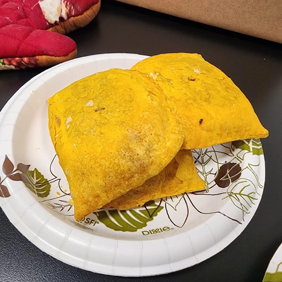 Three golden-yellow Jamaican patties, filled with savory ingredients, on a white paper plate.