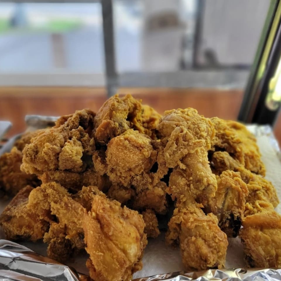 A large pile of golden-brown fried chicken pieces on a foil-lined tray at OSU Jerk Grill.