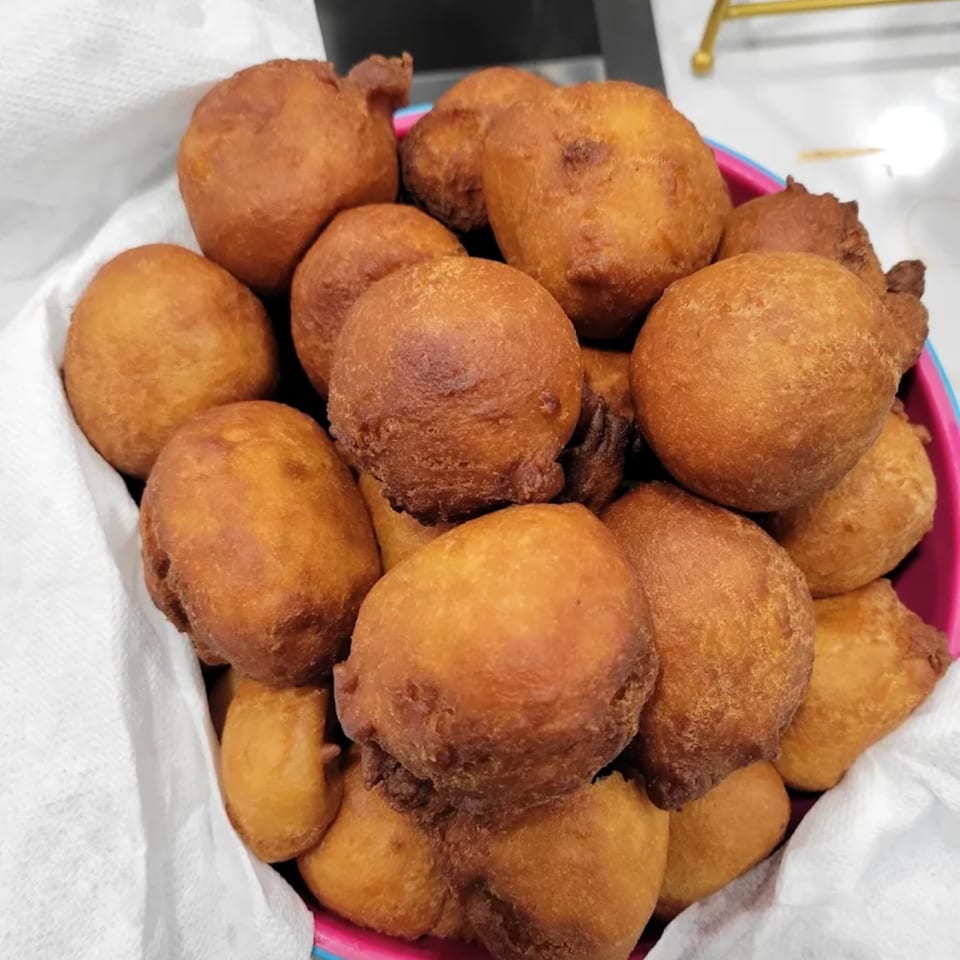 A pink bowl filled with golden-brown, Caribbean-style fried dumplings, lined with a white paper towel.