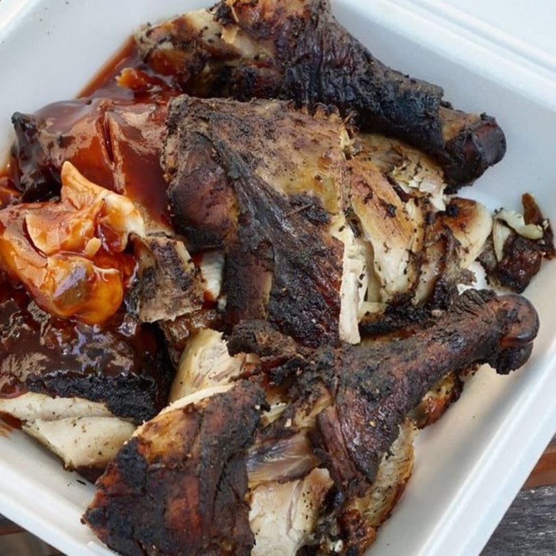 Close-up of OSU Jerk Grill's jerk chicken pieces with dark, crispy skin and a rich sauce.