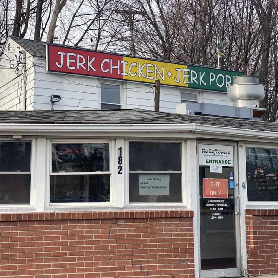 Exterior of OSU Jerk Grill, a white building with a colorful "Jerk Chicken Jerk Pork" sign.