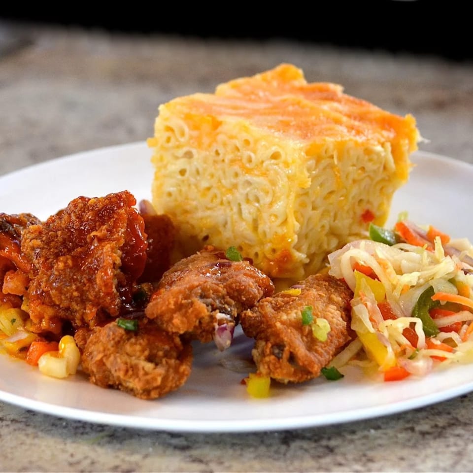 A plate of OSU Jerk Grill's fried chicken, baked macaroni and cheese, and colorful coleslaw.