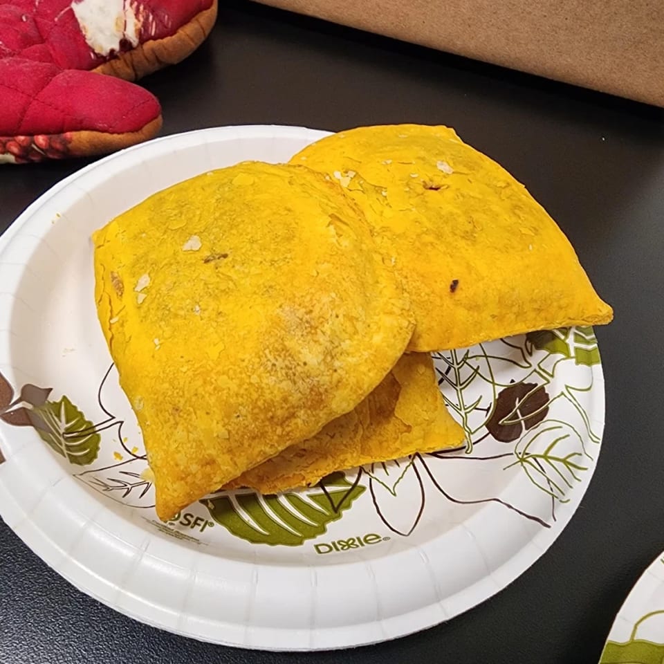 Two golden Jamaican beef patties on a white paper plate with green and brown leaf designs.