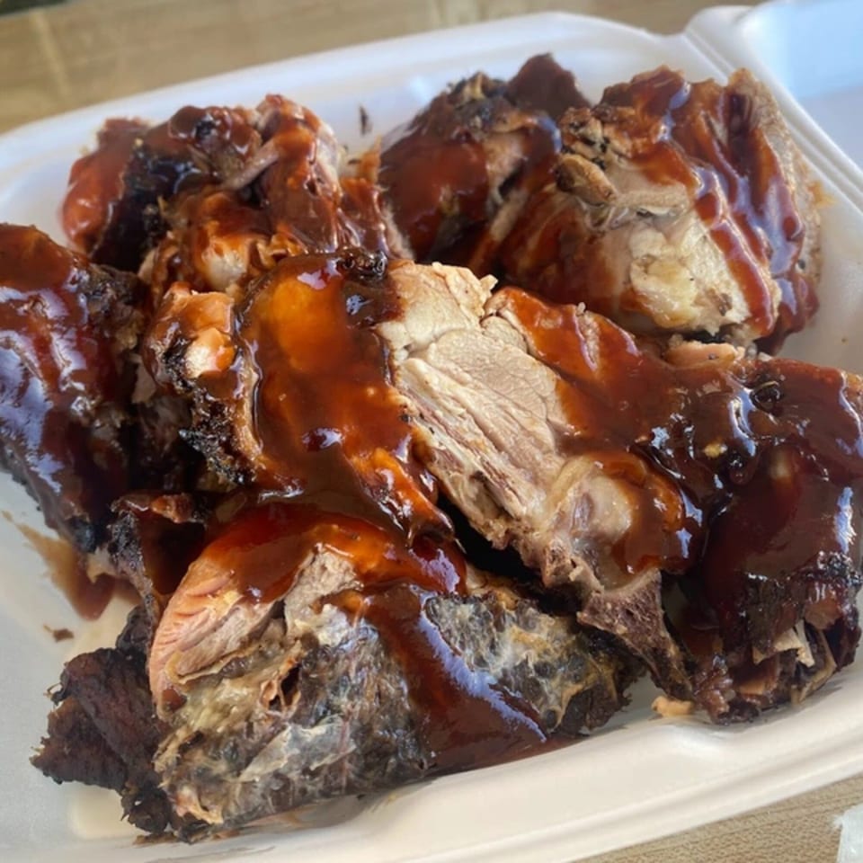 Close-up of OSU Jerk Grill's jerk chicken pieces, generously drizzled with a rich brown sauce in a white container.