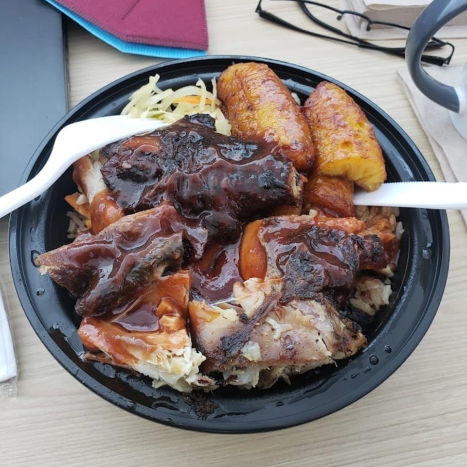 OSU Jerk Grill's jerk chicken with plantains and rice in a black takeout bowl.