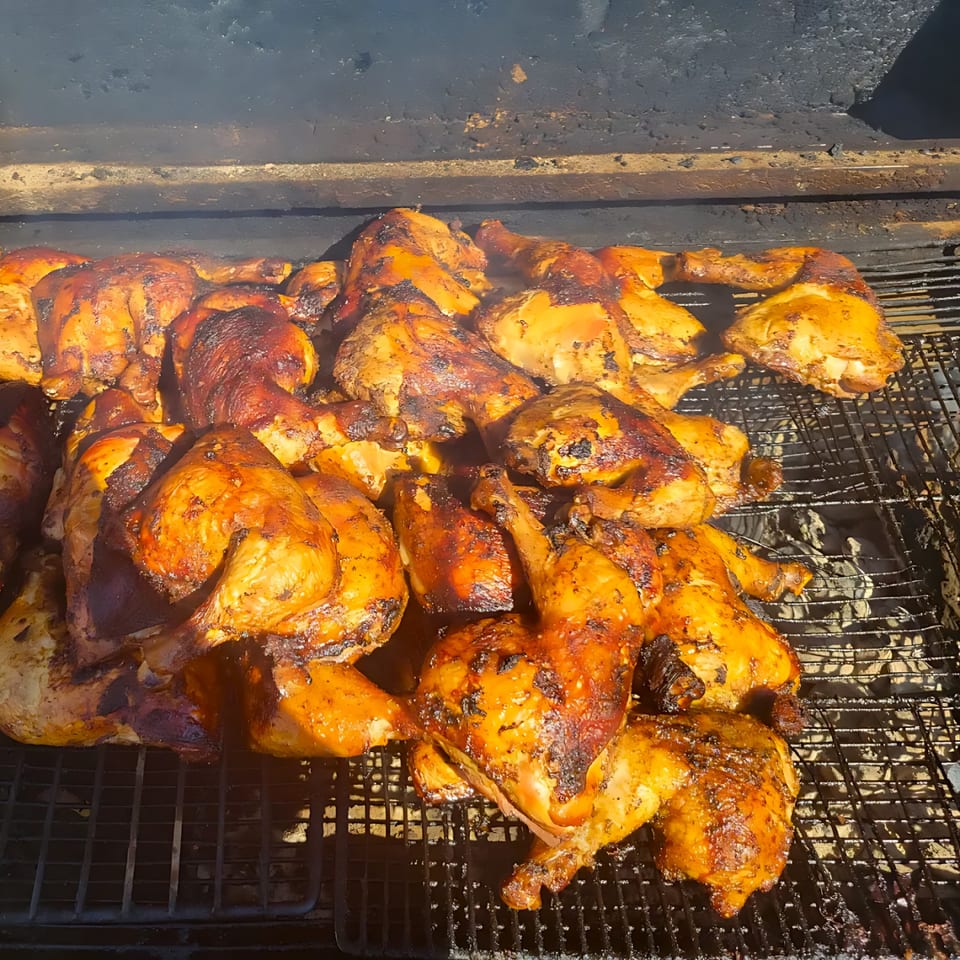Many pieces of jerk chicken with crispy skin cooking on a large grill.