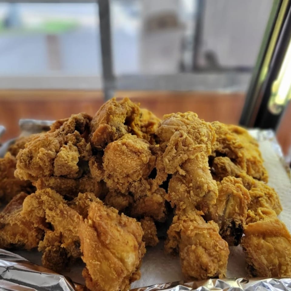 A large pile of golden-brown fried chicken pieces on a foil-lined tray.